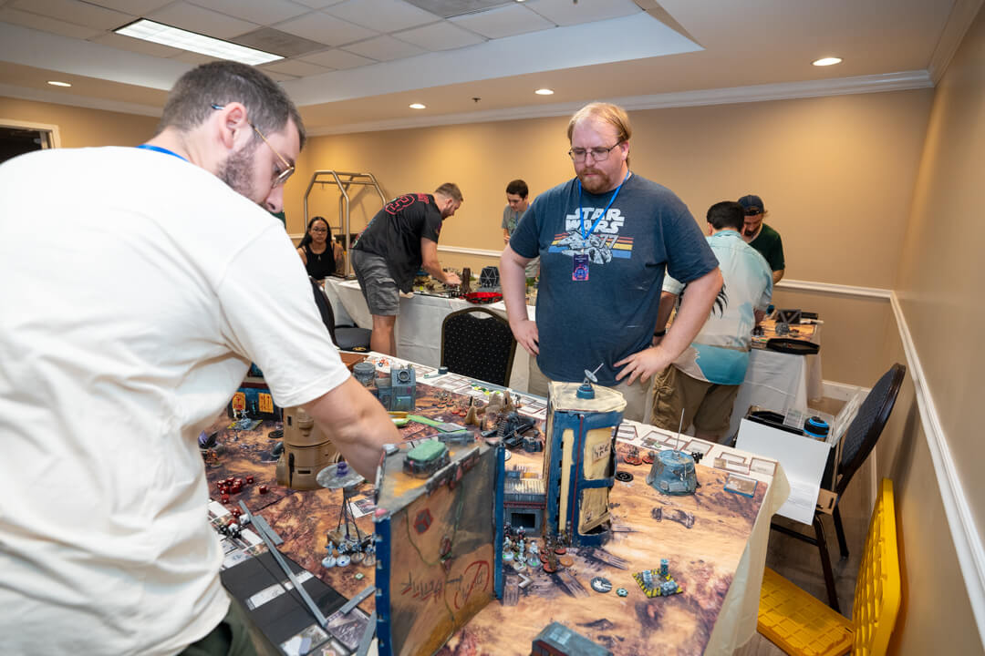 Dsc08742 Wicked Dicey Group of People Playing a Tabletop Miniature Wargame in a Conference Room Detailed Terrain and Miniatures on a Desert style Battle Mat on the Table