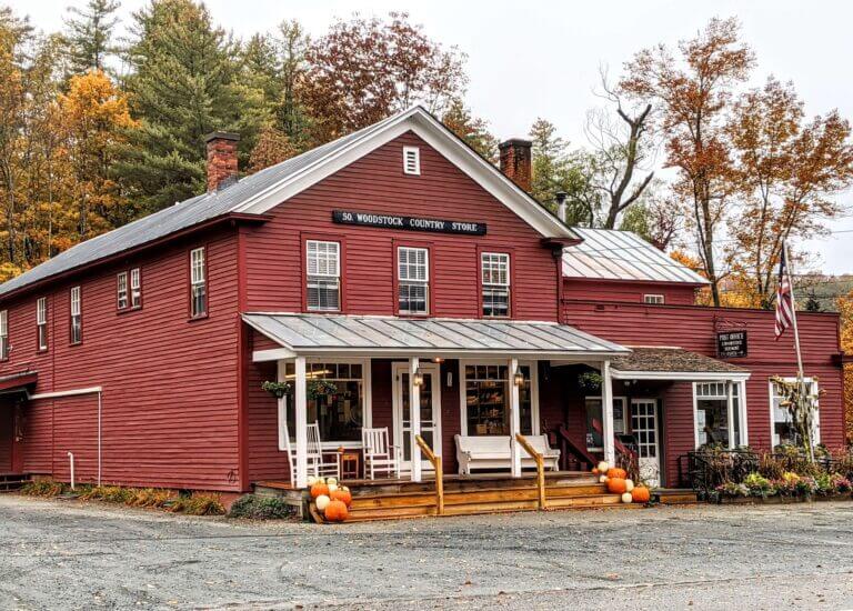 Red Wooden Country Store with a Wraparound Porch in Fall Colors and Pumpkins on the Steps by the Entrance