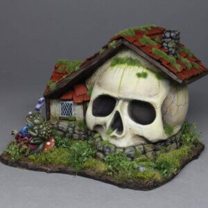 Skull-shaped house with red mossy roof, stone foundation, and overgrown yard; a colorful creature sits nearby, creating a eerie fantasy scene