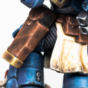 Close-up of a blue armored action figure with brown utility pouches and a worn beige tunic.