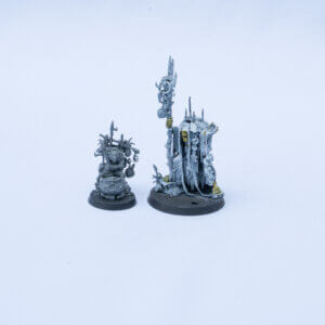 Two pale gray fantasy miniatures: a tall cloaked figure with a spiked crown and ornate staff, and a smaller gear-covered companion on a round base.